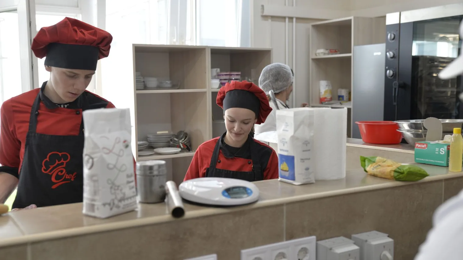 Deux apprentis en toque et tablier de cuisine s'entraînant sur un poste de préparation, formation rémunérée en alternance