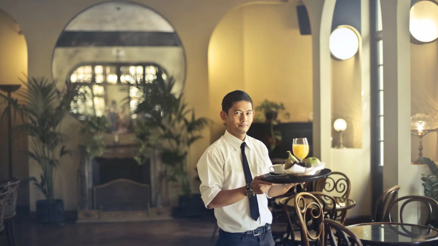 Jeune employé polyvalent en restauration portant un plateau de service, tenue professionnelle